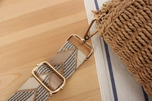 Detail of adjustable geometric woven shoulder strap with gold hardware on a straw bag