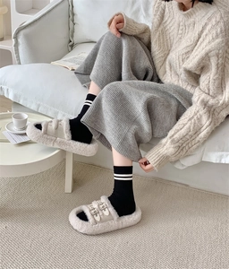 Close-up of beige plush slippers with double buckle straps and black striped wool socks