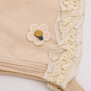 Beige baby knit hat with crochet flower and white lace trim detail in a soft handmade style