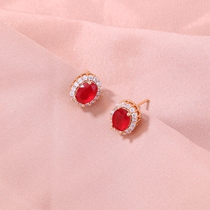 Detailed close-up of oval red gemstone earrings with white zircon halo in rose gold