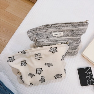 Detail of minimalist fabric makeup bags in cream embroidery and grey tweed textures
