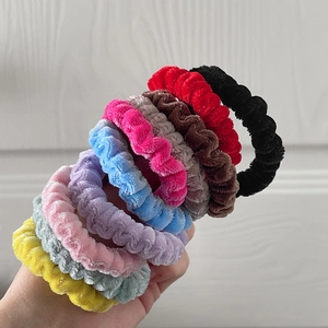 Set of nine colorful velvet scrunchies in various shades held for ponytail styling