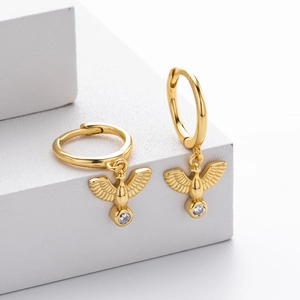 Detailed macro shot of gold dove earrings with sparkling zircon drop on white geometric stand