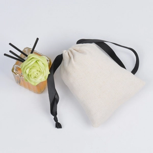 Close-up of beige linen jewelry pouch with black drawstring and amber glass bottle