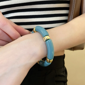 Detailed view of turquoise acrylic tube bracelet with gold metal spacer rings on a wrist