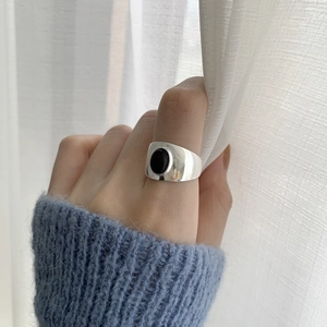 Detailed view of an S925 silver wide ring with black agate inlay worn against a white curtain