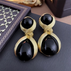 Close-up of vintage gold drop earrings with black stones and brushed metal texture