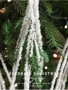 Close-up of white faux pearl sprays hanging on a green Christmas tree with warm bokeh