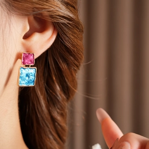 Close-up of square enamel earrings with pink and blue colors and golden hammered texture