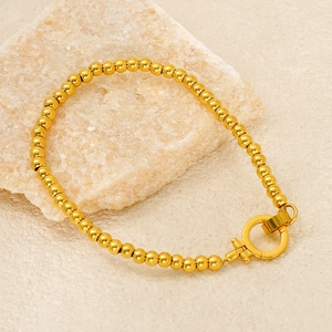 Golden stainless steel bead bracelet with round OT toggle clasp on marble background