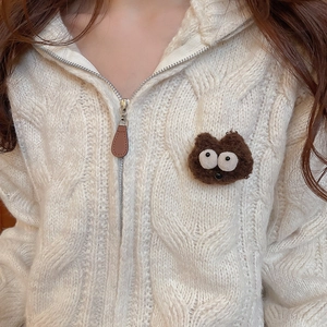 Detail of cable knit cardigan featuring a plush cartoon monster patch and leather zipper pull
