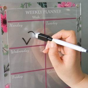 Close-up of hand writing on clear acrylic weekly planner board with black marker