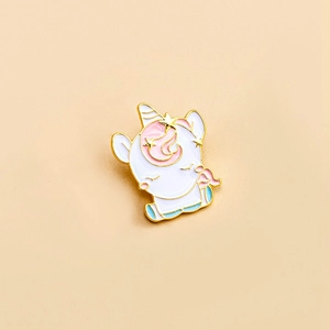 Cute cartoon unicorn enamel pin in white and pink with gold plating on beige background