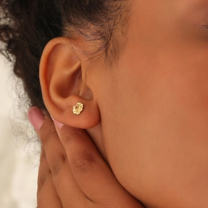Golden flower stud earrings with a tiny red gemstone detail on a female model's ear