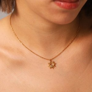 Golden stainless steel sunburst necklace set with sparkling crystal worn by a model