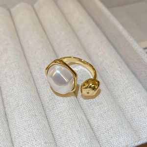 Macro view of gold-plated ring with irregular pearl on beige textured jewelry box