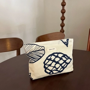 Close-up of cream canvas cosmetic bag with dark blue leaf patterns on a wooden table
