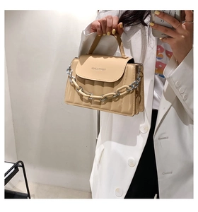 Detail of beige quilted leather handbag featuring metal chain strap and top handle