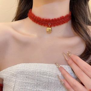 Gros plan d'un choker en maille rouge avec pendentif cloche dorée sur du tweed blanc
