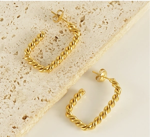 Close-up of gold twist hoop earrings with detailed spiral texture on beige stone