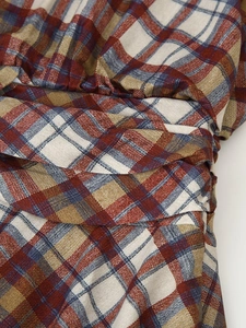 Macro shot of rust red and navy plaid fabric texture with detailed smocked stitching