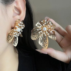 Detailed view of large gold floral earrings with pearl center worn by a model