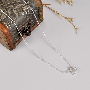 Close-up of silver scallop shell pendant on a smooth snake chain against vintage decor