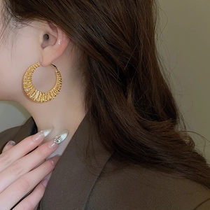Detail of model wearing large gold hollow twist hoop earrings with luxury moon texture