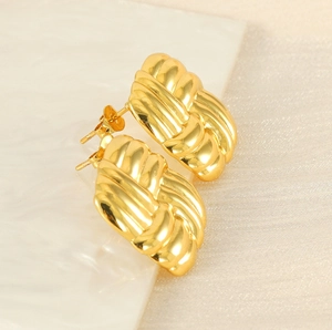 Macro shot of gold textured croissant earrings on a beige satin background