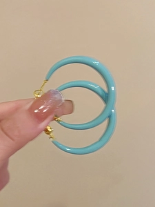 Detailed macro of a lake blue C-shaped oil-dripping hoop earring held in hand
