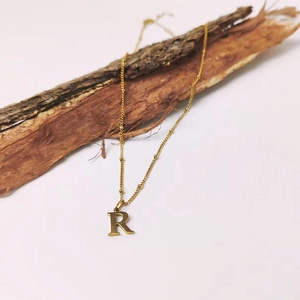 Détail d'un collier chaîne à billes doré avec un pendentif minimaliste de la lettre R