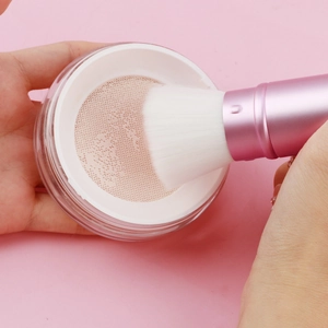 Detail of soft cat claw powder brush dipping into a loose powder container