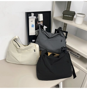 Three minimalist nylon crossbody hobo bags in white, grey, and black on a modern table