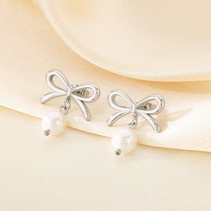 Macro detail of silver bow stud earrings with white pearls on elegant silk background