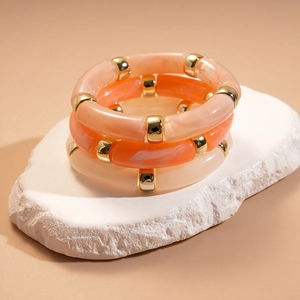 Détail de trois bracelets joncs en acrylique marbré avec des perles dorées en métal