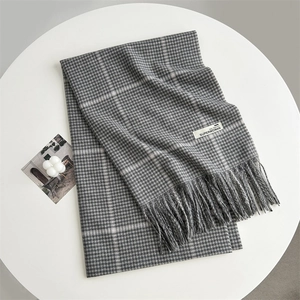 Detail of grey houndstooth scarf featuring a fringe edge and SUPERWOMAN brand tag