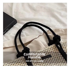 Detail of woven straw tote bag featuring thick black rope handles and knotted design