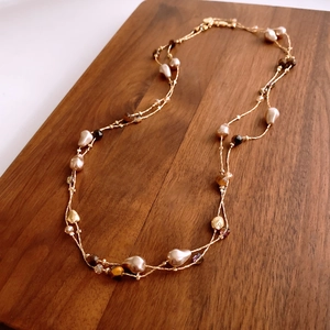 Detail of baroque pearl and tiger eye stone necklace on a dark brown wooden background
