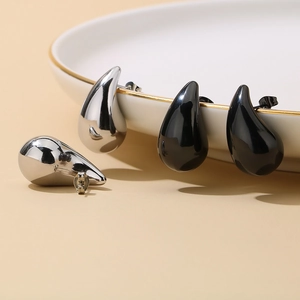 Macro detail of teardrop stud earrings in silver and black finishes on a white plate