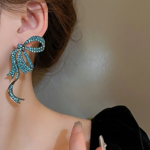 Detailed view of model wearing a large blue rhinestone bow earring with ribbon design
