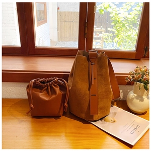 Detail of a large brown suede tote bag and matching drawstring pouch on a wooden ledge