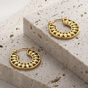 Close-up of golden hollow leaf patterns on stainless steel hoop earrings on stone
