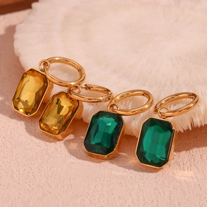 Detail of 18K gold earrings with amber and emerald rectangular cut zircon gems on white stone