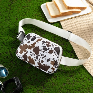 Detail shot of a lightweight cow print waist bag placed on a green picnic setting.