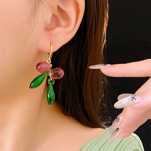 Gros plan sur des boucles d'oreilles cerise en verre avec perles rouges et feuilles vertes