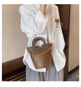 Detail of brown faux leather bucket bag with amber acrylic chain and round handle