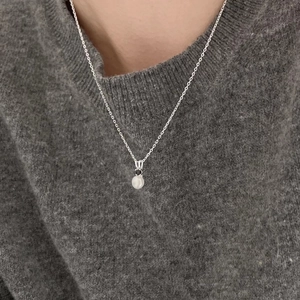 Close-up of minimalist 925 sterling silver necklace with pearl pendant on a knit sweater