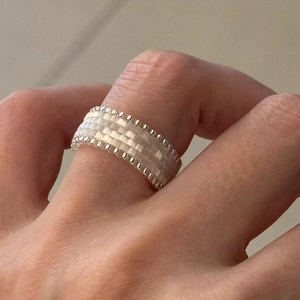 Detailed view of a handmade cream bead woven wide ring with silver metallic bead edges