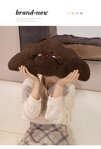 Close-up of soft brown croissant plush pillow with cute embroidered face on a sofa