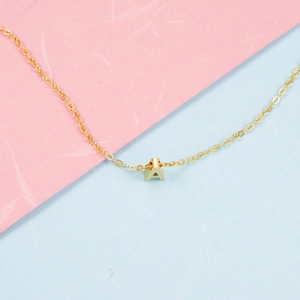 Polished gold initial A pendant necklace with stainless steel chain on a pastel background